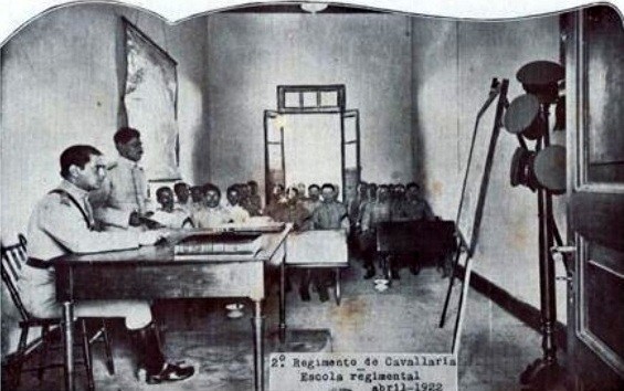 Oficiais e alunos uniformizados em uma sala de aula na Escola Regimental do º RC