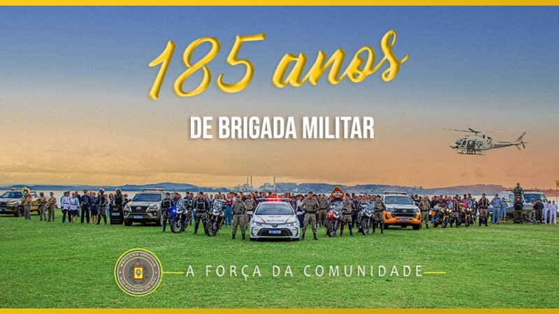 Grande grupo de militares fardados reunidos na beira de um rio, sob um gramado verde. Acompanhados por viaturas, motocicletas e um helicóptero realizando sobrevoo.