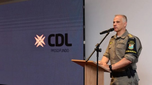 Imagem mostra comandante do CRPO-Planalto, da Brigada Militar, discursando em frente a púlpito, com um telão com a logo da CDL Passo Fundo por trás