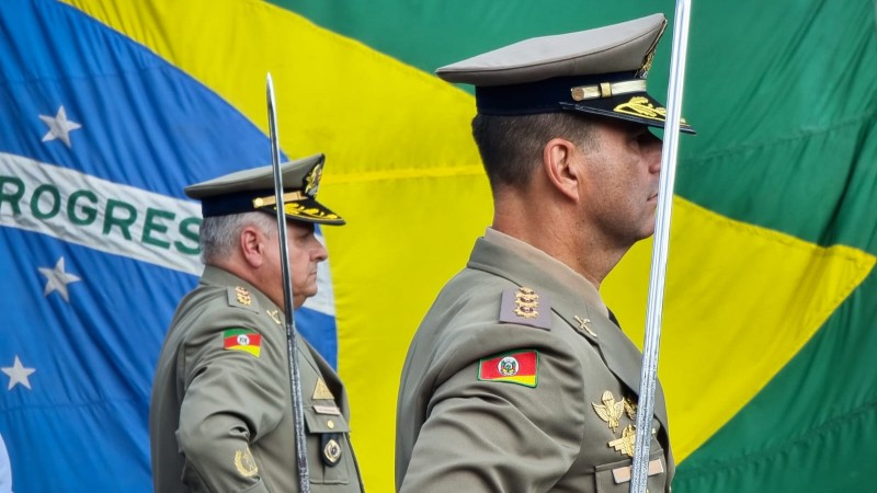 Em primeiro plano, foto mostra dois coronéis perfilados com espadas nas mãos. Em segundo plano, bandeira do Brasil.