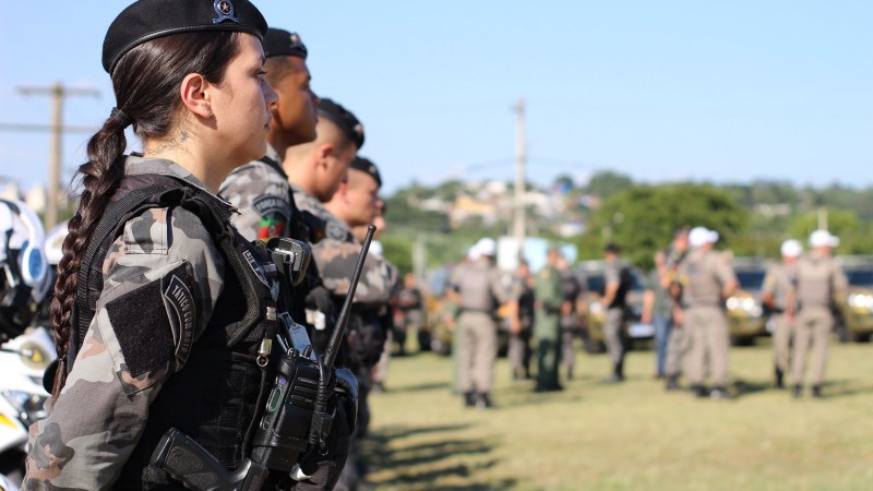 Foto mostra soldados da Brigada Militar enfileirados em campo aberto em um dia ensolarado.