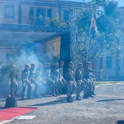Foto mostra formandos marchando na entrada da formatura, em meio a uma cortina de fumaça