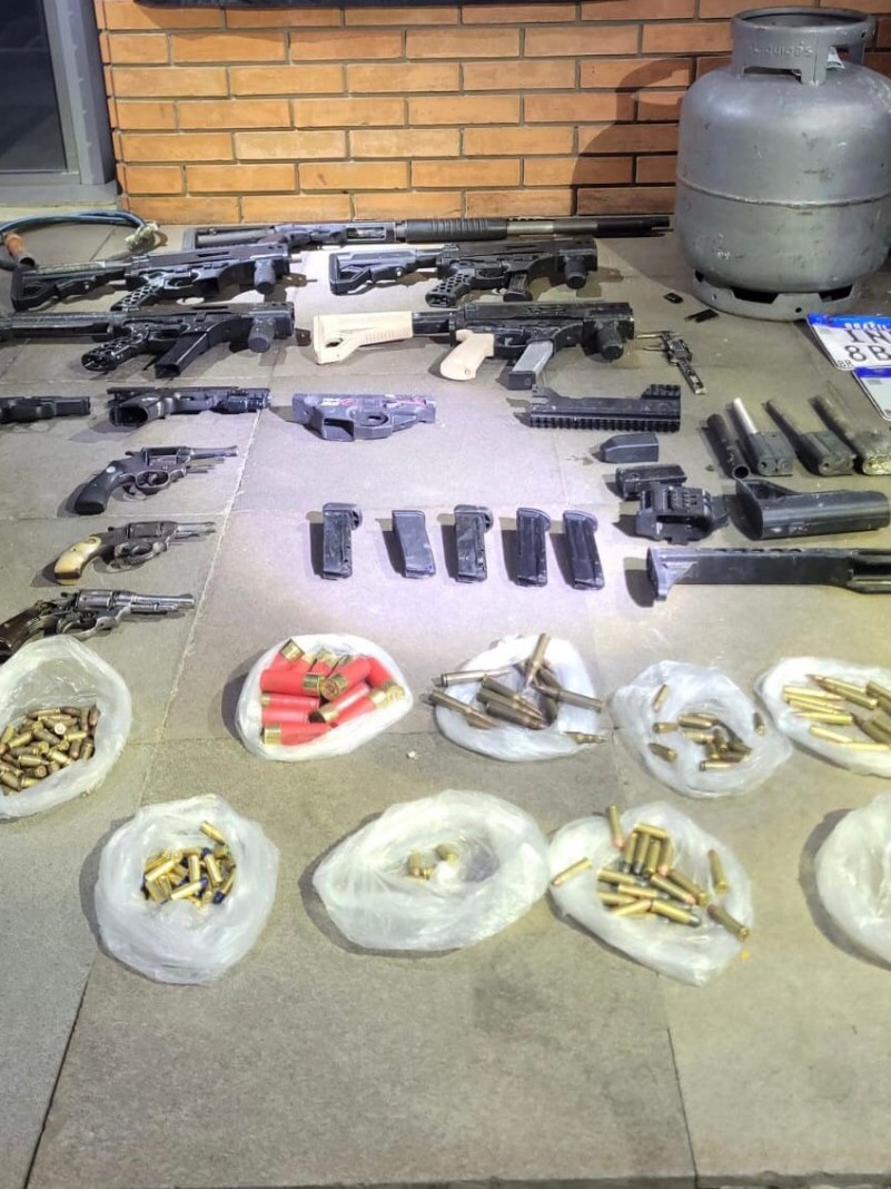 Imagem mostra diversas armas de fogo, carregadores e munições distribuídas no chão.