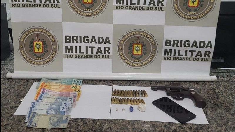 Arma apreendida, drogas, dinheiro e munições em cima de uma mesa.