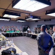 Foto mostra mesa de reunião com coronéis em pé durante apresentação