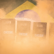 Imagem mostra a entrada dos formandos, que estão segurando escudos do choque em meio à fumaça laranja. Por trás, a bandeira do Brasil