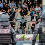 Imagem mostra, em primeiro plano, dois soldados do Choque de costas. Em segundo plano, em um palanque, o Comando da BM prestigia a cerimônia