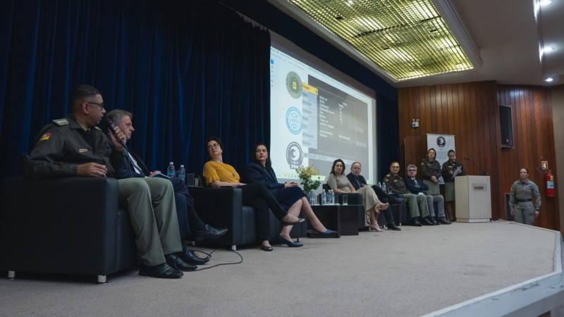 Imagem mostra participantes sentados em um palco, palestrando durante o evento