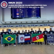 Foto mostra os alunos enfileirados no embarque do aeroporto, segurando as bandeiras do Brasil, do Colégio Tiradentes e do Rio Grande do Sul