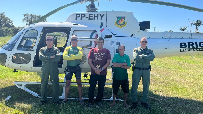 Foto mostra integrantes do Batalhão de Aviação junto aos resgatados, na frente a um helicóptero