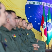 Foto mostra os formandos sentados em fileira. Em segundo plano, estão as bandeiras do Brasil, do Rio Grande do Sul e da Aviação da Brigada Militar.