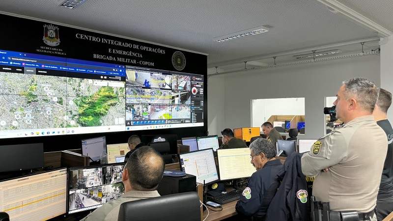 Foto mostra o comandante do Copom na sala de monitoramento assistindo às câmeras da cidade espelhadas em um grande monitor