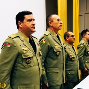 Foto mostra quatro oficiais da BM perfilados em uma mesa, em posição de respeito, durante a execução de hino.