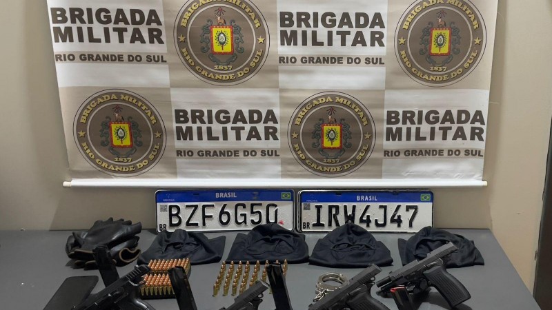 Armas, placas de veículos, munições, luvas, celular sobre uma mesa eo brasão da BM
