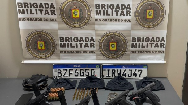 Armas, placas de veículos, munições, luvas, celular sobre uma mesa eo brasão da BM
