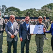 No campo do estádio, aparecem da esquerda para a direita, o Comandante-Geral, o Secretário de Segurança Pública, o Vice-Governador, a Soldado PM condecorada e seu padrinho. 