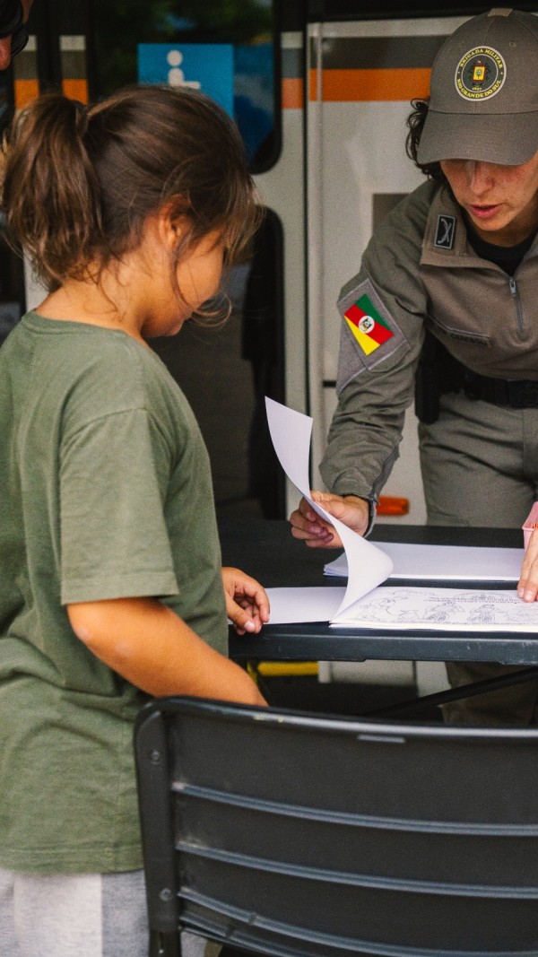 PM feminina dialoga com uma criança à mesa de desenho e de leitura.