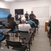 Cinco PMs aparecem em pé e diante de torcedores presentes na sala. 