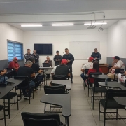 Em uma sala, seis PMs falam em pé e diante de torcedores sentados.  