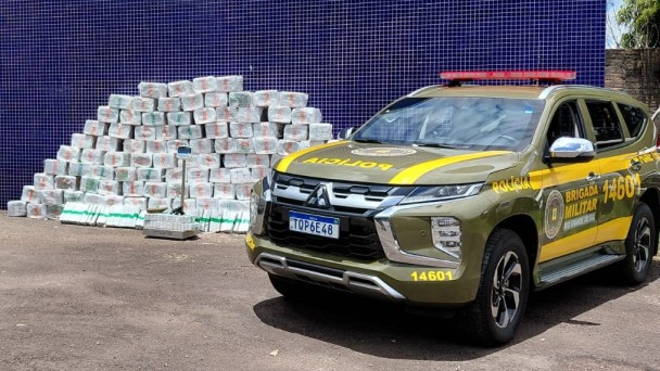 Uma viatura da BM aparece ao lado da pilha em formato de pir&acirc;mide de embalagens de maconha. 