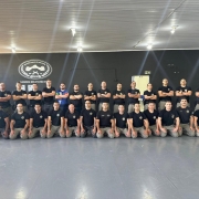 Foto mostra os instrutores que participaram do nivelamento todos reunidos em duas fileiras em cima de um tatame dentro de um gin&aacute;sio