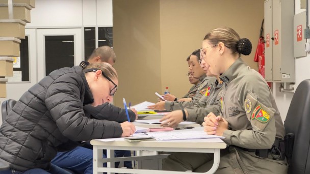 Candidatos ao Curso Superior de Pol&iacute;cia Militar preenchem formul&aacute;rios enquanto s&atilde;o atendidos por policiais militares do Departamento de Pessoal e Finan&ccedil;as. A atividade ocorre em uma mesa de confer&ecirc;ncia documental.