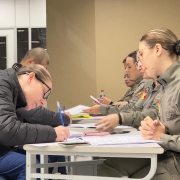 Candidatos ao Curso Superior de Pol&iacute;cia Militar preenchem formul&aacute;rios enquanto s&atilde;o atendidos por policiais militares do Departamento de Pessoal e Finan&ccedil;as. A atividade ocorre em uma mesa de confer&ecirc;ncia documental.
